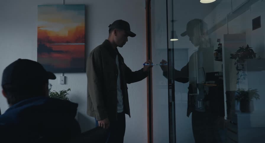 A man leads a creative brainstorming session, writing ideas on a glass wall in a modern, dimly lit office