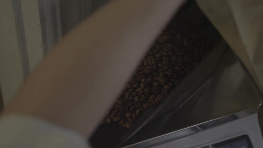 A man is pouring coffee beans into a container on a scale