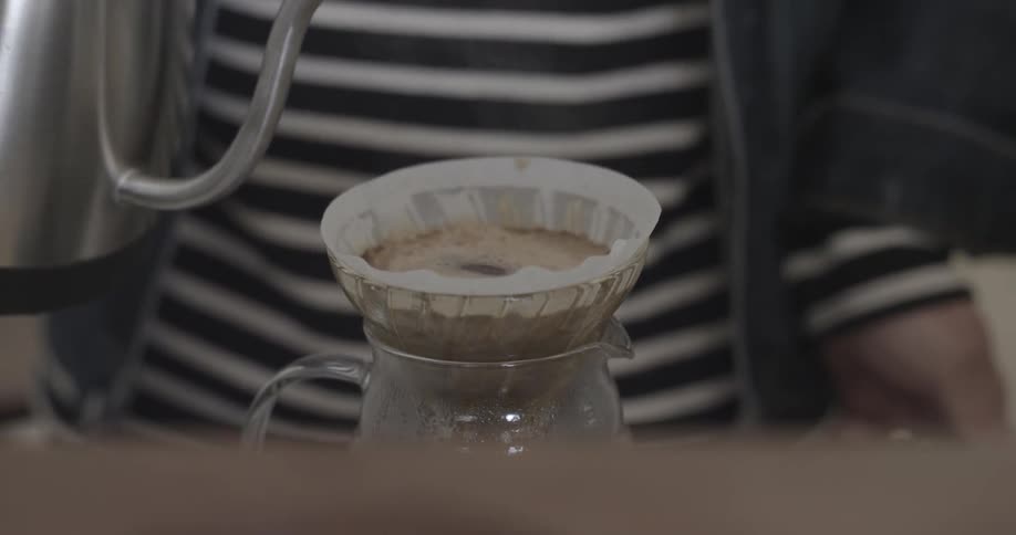 A woman is pouring water over coffee grounds in a filter