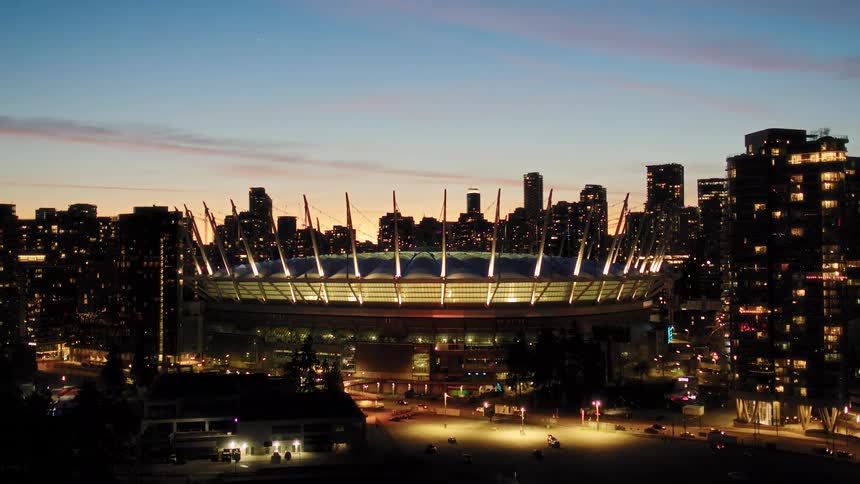 A stunning aerial view of the illuminated BC Place stadium set against the Vancouver city skyline at twilight