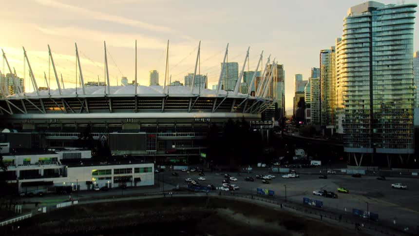 Aerial shot rises from the water to reveal BC Place stadium and the Vancouver skyline at sunset