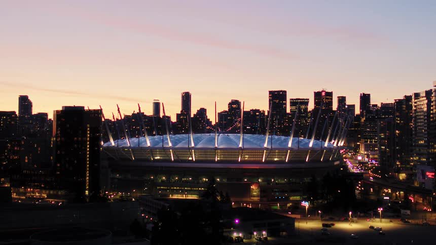 Vancouver's cityscape glows at dusk, featuring the illuminated BC Place stadium against a colorful sunset sky