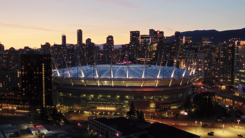 Aerial view of the illuminated BC Place stadium against the glowing Vancouver skyline at dusk