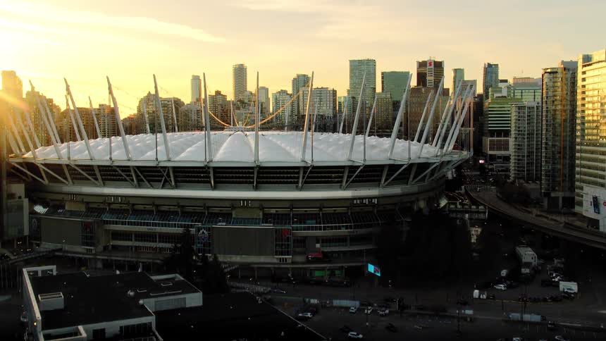 An aerial view rises from the water to reveal the iconic BC Place stadium and the stunning Vancouver city skyline at golden hour