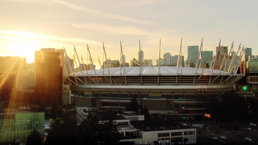 A dramatic aerial reveal tilts up from the shimmering waters of False Creek to unveil the iconic BC Place stadium and the Vancouver skyline glowing at sunset