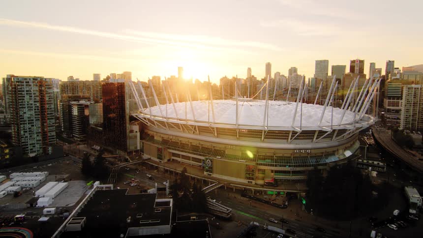 A stunning aerial reveal of BC Place stadium and the Vancouver city skyline glowing in the golden light of sunset