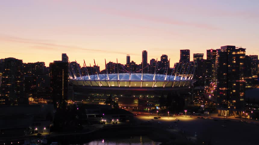 Aerial view of the iconic BC Place stadium illuminated against the downtown Vancouver city skyline at dusk