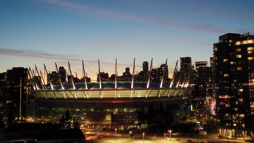 An aerial reveal of Vancouver's BC Place stadium beautifully illuminated against the city skyline at dusk