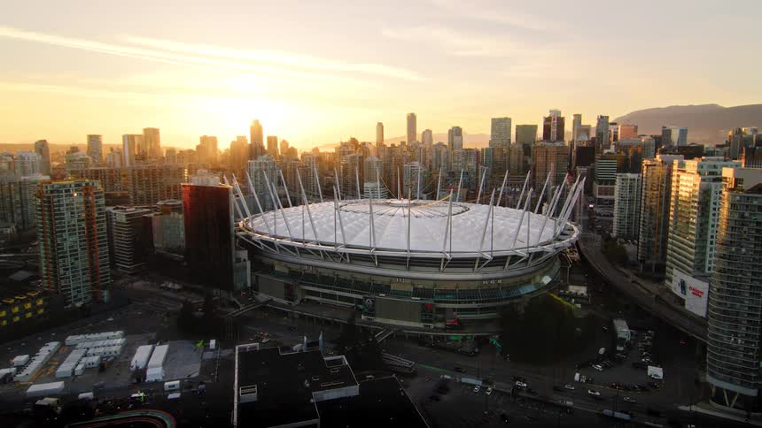 A breathtaking aerial shot reveals the Vancouver cityscape and BC Place stadium, beautifully illuminated by the setting sun