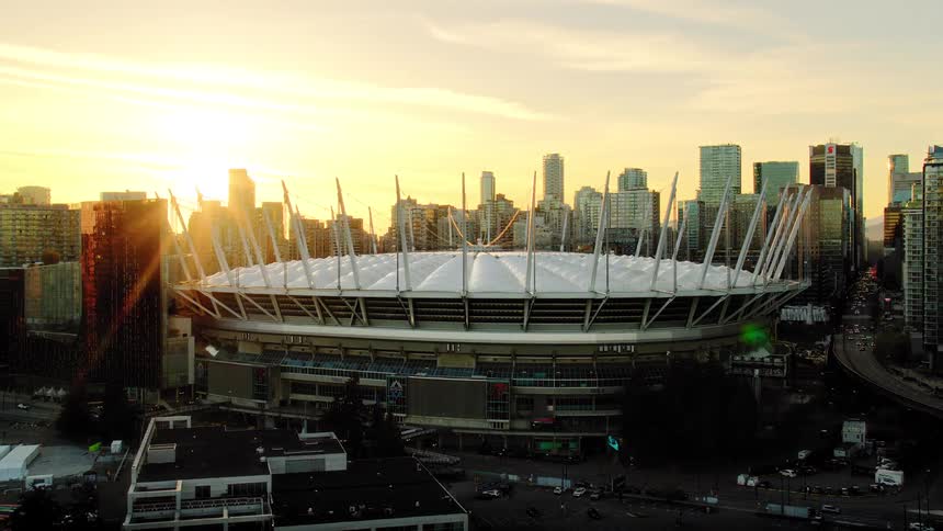 An aerial view slowly pushing in on BC Place stadium in Vancouver as the city is bathed in the warm glow of sunset