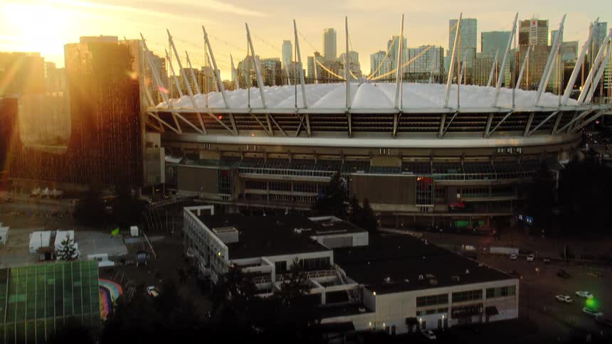 An aerial shot tilts up from a dark marina to reveal the iconic BC Place stadium and Vancouver skyline at golden hour