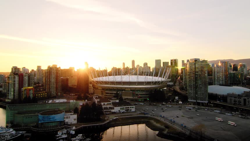 An aerial view of the Vancouver skyline and BC Place stadium as the sun rises, casting a golden glow over the city