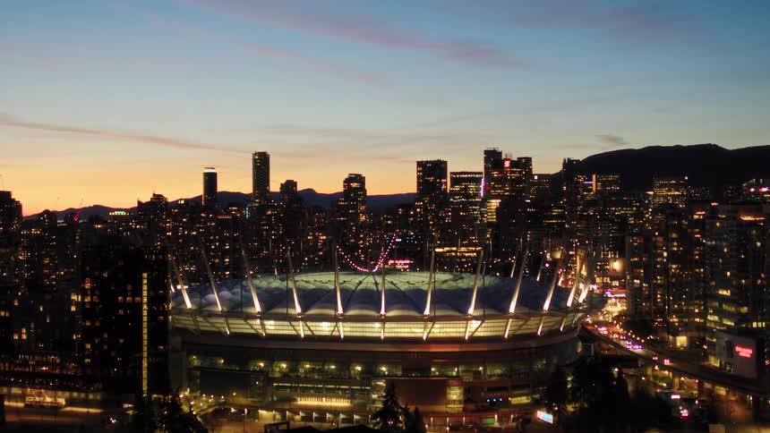 A stunning aerial view captures the illuminated BC Place stadium and the vibrant Vancouver city skyline at dusk