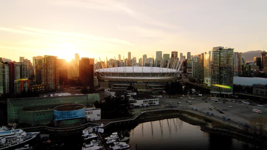 A breathtaking aerial pullback reveals BC Place stadium amidst the glowing Vancouver skyline at sunset