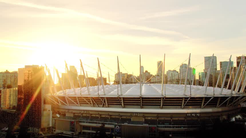 Tilting up from the shimmering water to reveal Vancouver's iconic BC Place stadium glowing in the golden light of sunset