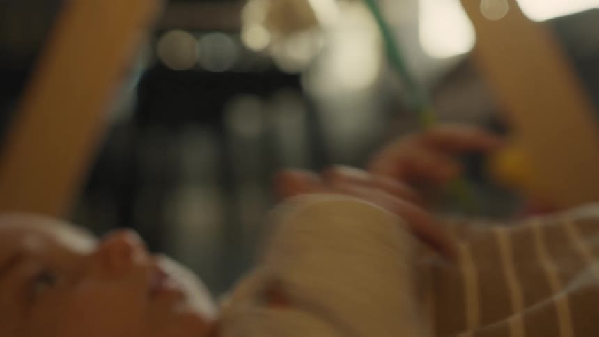 A gentle focus pull from a baby's tiny hand to its curious face as it lies peacefully under a play gym