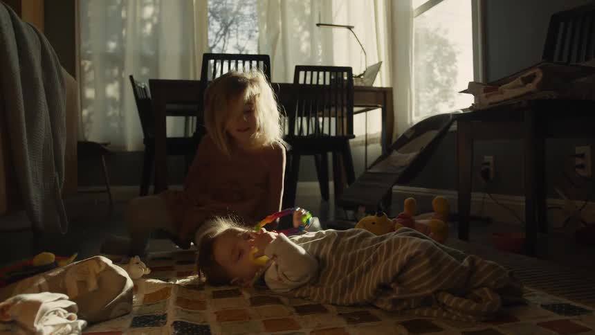 Slow motion shot of a happy toddler girl playing with her baby sibling on the floor in a warm, sunlit room