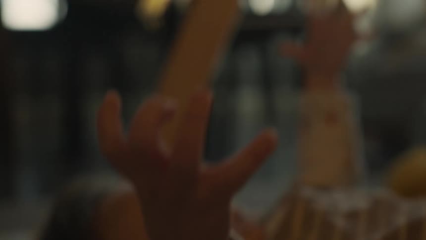 A baby's tiny hands reach up towards the warm light in a gentle, out-of-focus shot