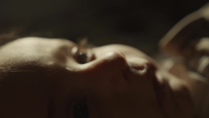 An intimate extreme close-up of a newborn baby's curious blue eye looking around while lying down in soft, warm light