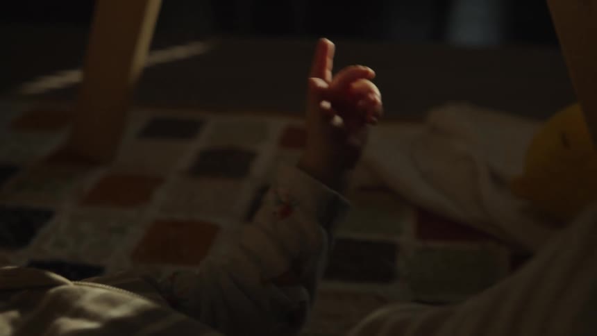 A cute baby bathed in sunlight lies on the floor playing with a toy in slow motion