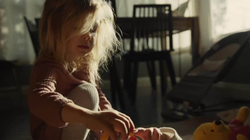 A big sister entertains her baby sibling with a colorful teether toy while playing on the floor in a sunlit room