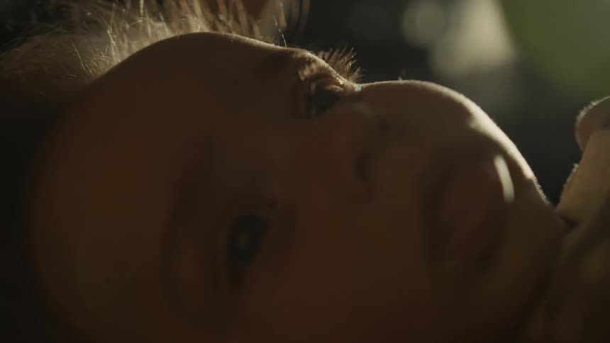An intimate macro shot of a newborn baby's face as their eyes slowly close and they drift off to sleep