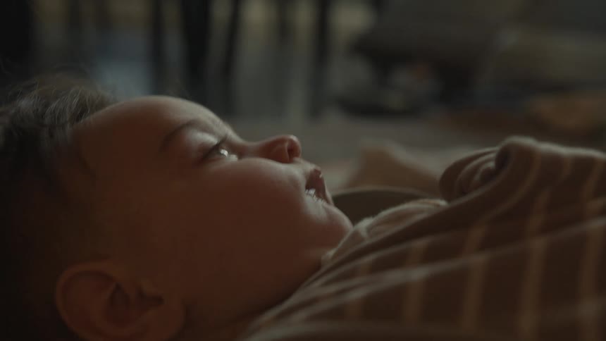 A slow focus pull reveals a close-up of a happy baby with chubby cheeks lying on its back and smiling