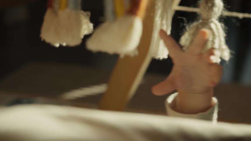 Close-up slow motion shot of a baby's tiny hand reaching for a hanging tassel toy