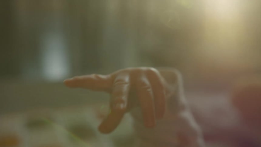A dreamy, out-of-focus close-up of a newborn baby's tiny hand reaching out in soft, warm light