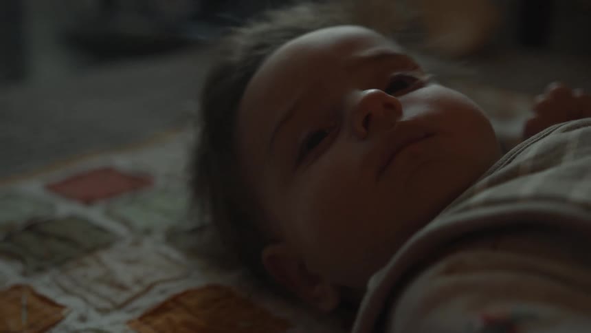 An adorable baby with messy hair lies awake and calm on a soft blanket