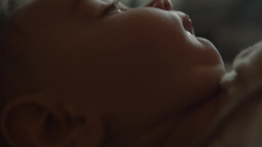 A dreamy, intimate close-up shows a newborn baby's face as they peacefully lie awake