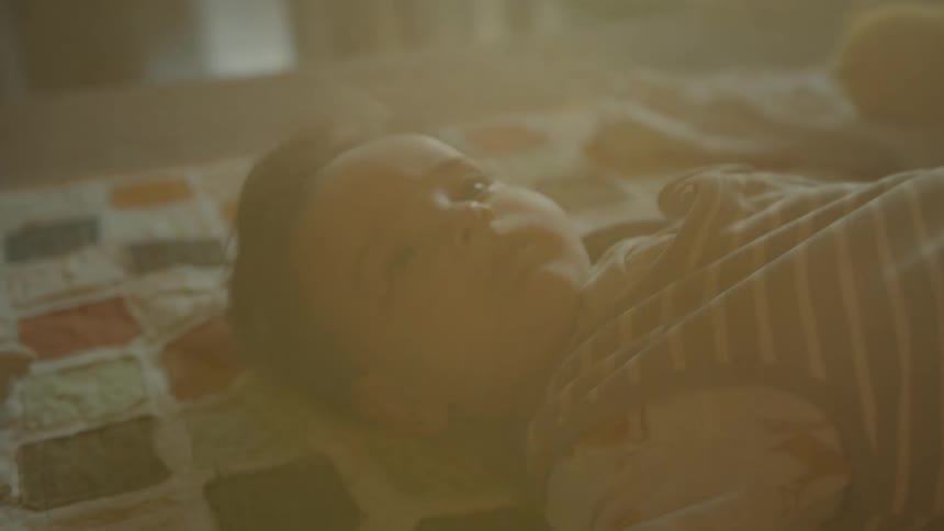 A serene close-up of a baby lying peacefully on a quilt, bathed in the warm, hazy glow of sunlight