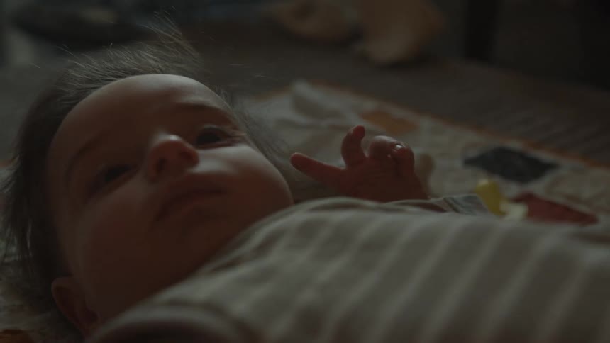 Softly lit close-up of a peaceful newborn baby lying on a quilt and looking up thoughtfully