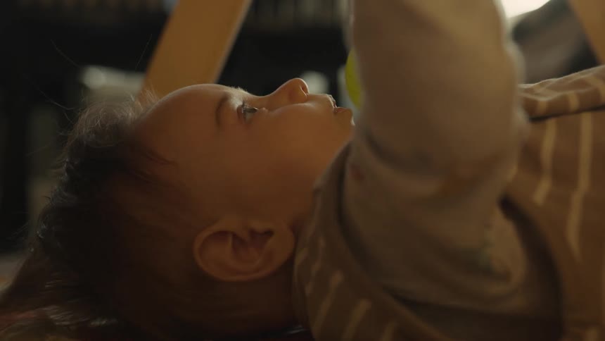 A close-up shot of a baby lying on its back, happily chewing on a hanging teething ring