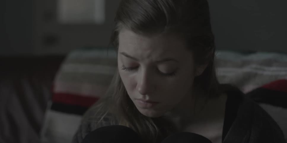 A woman looks sad in a bedroom, and drinks from a mug