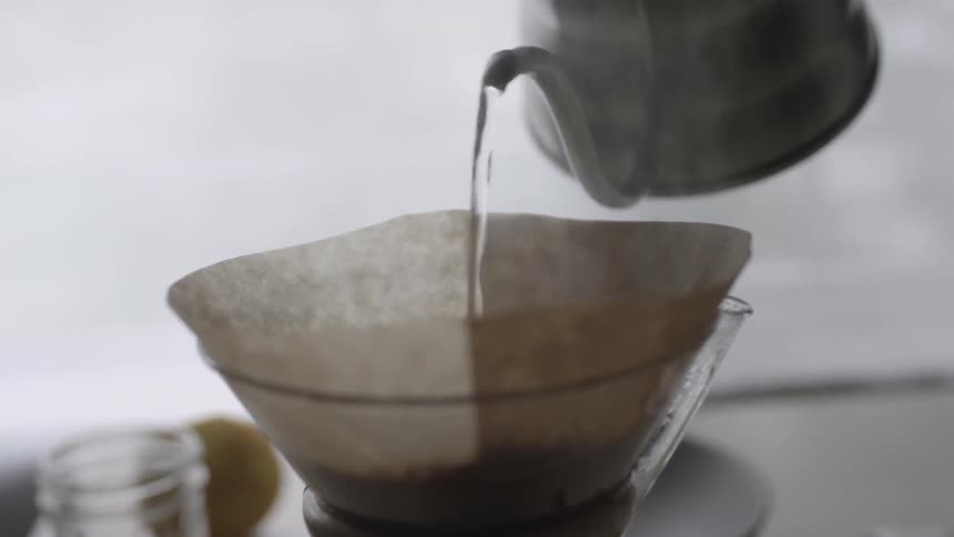 Water from a silver kettle is poured over coffee grounds