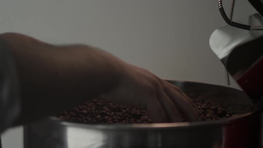 A man is sifting through coffee beans in a roasting pan
