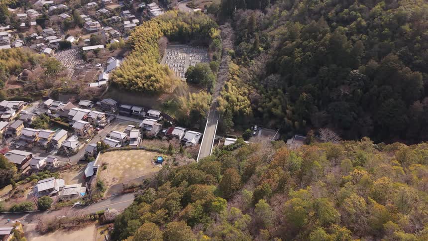 An aerial timelapse captures the changing daylight over a quaint Japanese village nestled between a forest and a bamboo grove