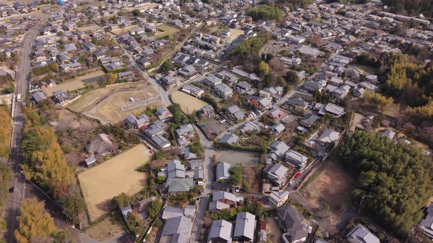 Slowly tilting up from a top-down aerial view of a small Japanese village to reveal the expansive city of Kyoto in the background