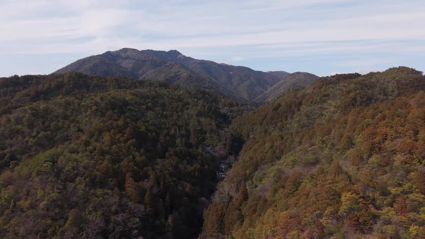 A wide, static aerial shot reveals a deep, tree-covered valley cutting through a vast mountain range