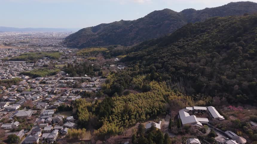 A slow aerial pullback reveals a picturesque Japanese town and a bamboo forest at the base of a lush mountain range