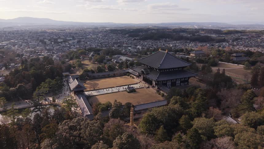A static aerial view shows the magnificent Todai-ji Temple in Nara, Japan, with tourists exploring the grounds and the city sprawling in the background