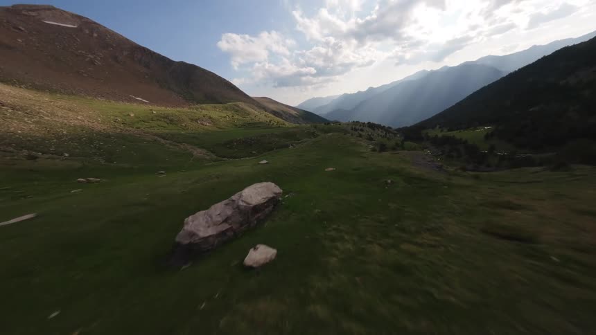 A thrilling FPV drone flight soars low over a lush green mountain valley with dramatic sun rays in the background