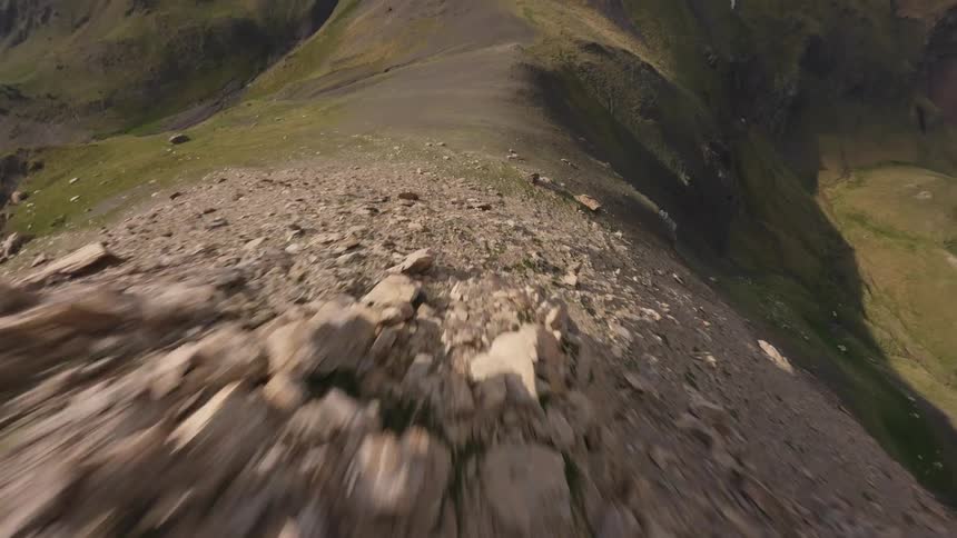 An exhilarating first-person view drone flight soars rapidly along a narrow, rocky mountain ridge towards a distant peak