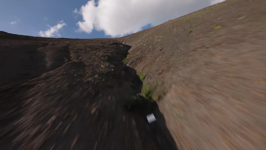 An FPV drone soars at high speed up the steep, barren slope of a mountain, closely following a rocky ravine towards the sky