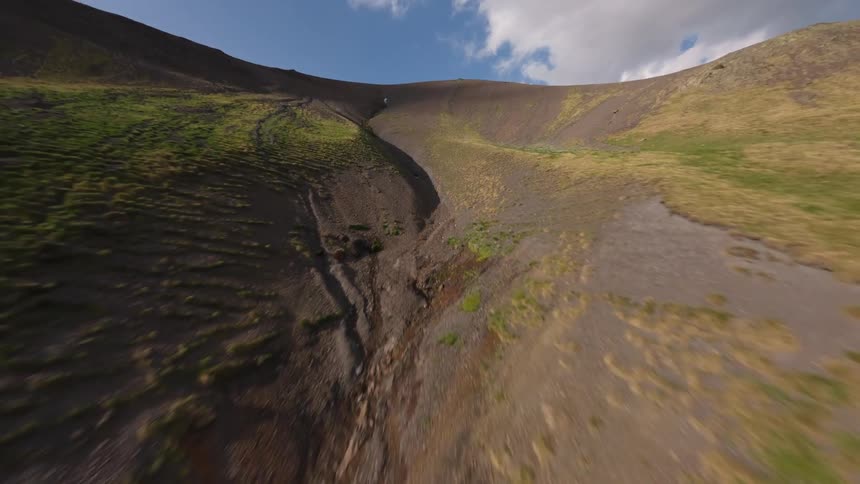 A fast-paced FPV drone pulls back rapidly up a rocky gully, revealing the rugged and barren mountain slope