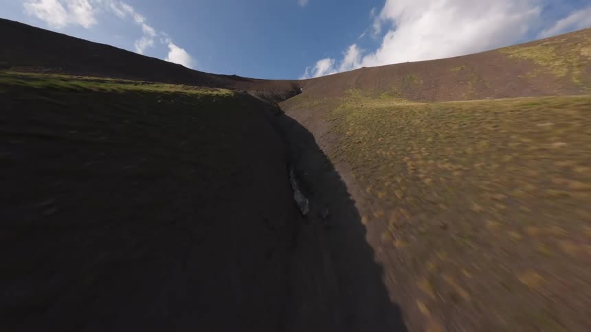 An exhilarating FPV drone flight soars up a rugged and steep mountain ravine toward a patch of snow at the summit