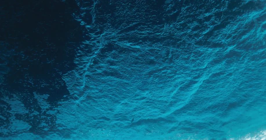 An underwater slow-motion view shows raindrops creating ripples on the deep blue water's surface