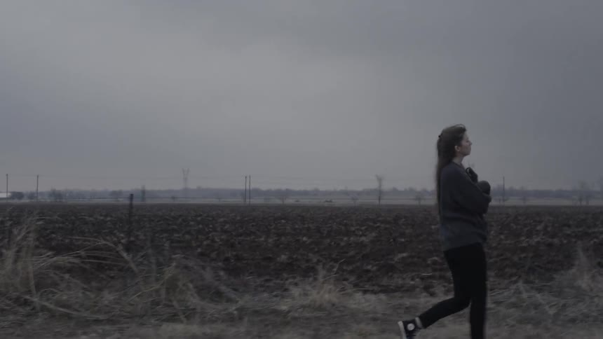 Woman walking out into a dry field on cloudy evening