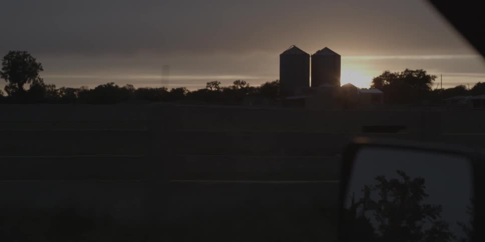 Traveling on country road with sun setting behind silos